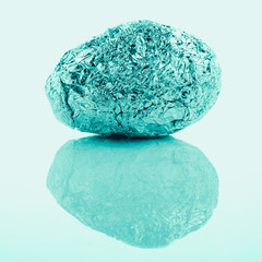crumpled aluminum foil ball in egg shape on plain background, sweet tone instragram like process