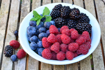 Raspberries, blue berries and black berries in a white bowl on a wooden garden table