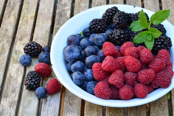 Raspberries, blue berries and black berries in a white bowl on a wooden garden table