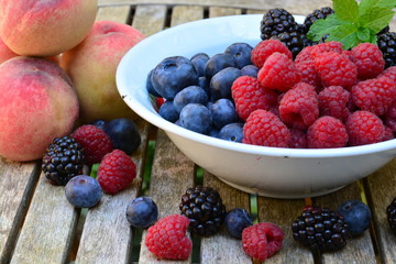 Raspberries, blue berries and black berries in a white bowl on a wooden garden table