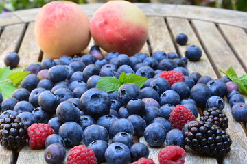 Peaches, raspberries, blue berries and black berries on a wooden garden table