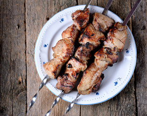 Home shish kebab from pork on skewers with pickled onion and parsley on an old wooden background.