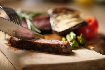 slicing medium rib eye steak with grilled vegetables
