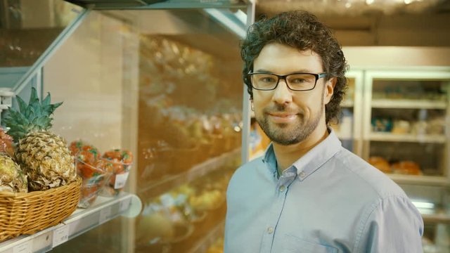 Portrait of young caucasian man in the glasses turning to the camera and smiling in the supermarket.