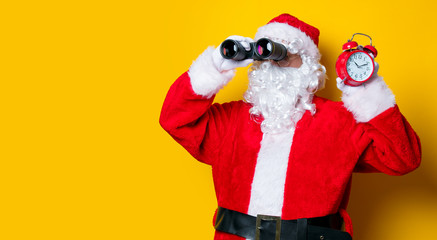 Santa Claus holding binoculars and alarm clock