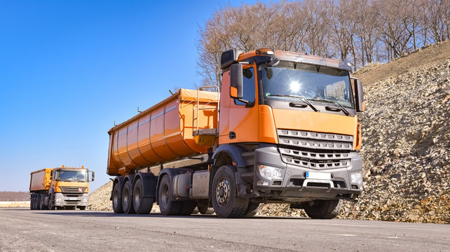 Zwei orange  LKW`s liefern Baumaterialien f&uuml;r eine neue Stra&szlig;endecke
