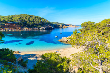 Fototapeta na wymiar Couple of unidentifed people sunbathing on beautiful beach in Cala Salada famous for its azure crystal clear sea water, Ibiza island, Spain