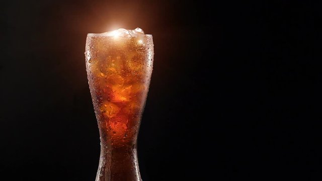Cold cola with ice in a glass on a black background