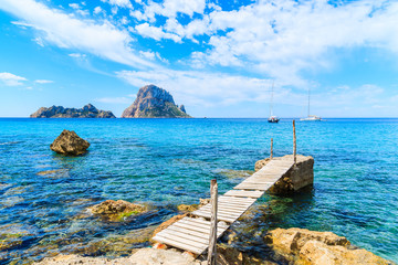 Small wooden pier in Cala d'Hort bay and view of Es Vedra island, Ibiza island, Spain