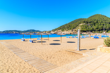 Sandy beach with umbrellas and sunbeds in Cala San Vicente bay on sunny summer day, Ibiza island, Spain