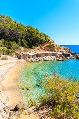 View of secluded Cala d'en Serra beach with boat houses on rocks, Ibiza island, Spain