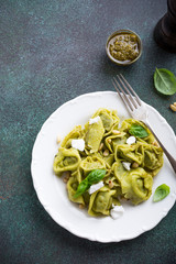Homemade Italian tortelloni with green pesto, goat cheese and pine nuts on white plate on green stone background. Healthy food concept. Copy space. High angle view.