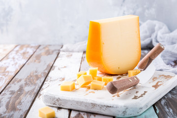 Delicious dutch gouda cheese with cheese cubes and special knife on old wooden table. Copy space. - obrazy, fototapety, plakaty