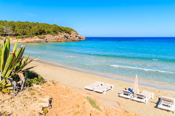Sunloungers on Cala Nova beach on sunny summer day, Ibiza island, Spain