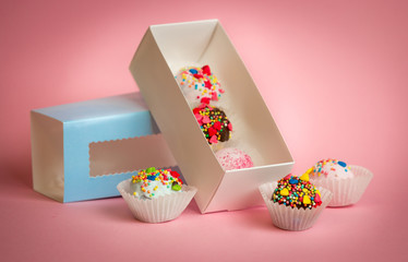 Open box with homemade cake balls with colorful sprinkles over pink background
