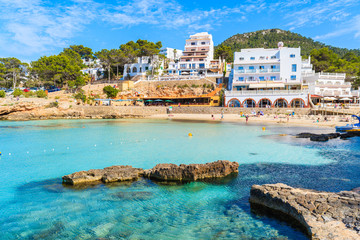Hotel and restaurant buildings in Cala Portinatx bay with azure blue sea water, Ibiza island, Spain