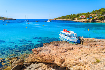 White and blue colour ferry boat for tourists mooring in Cala Portinatx bay, Ibiza island, Spain
