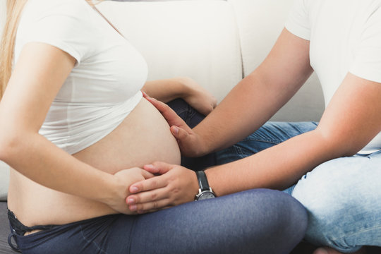 Closeup image of young couple expecting baby. Husband holding hands on big belly