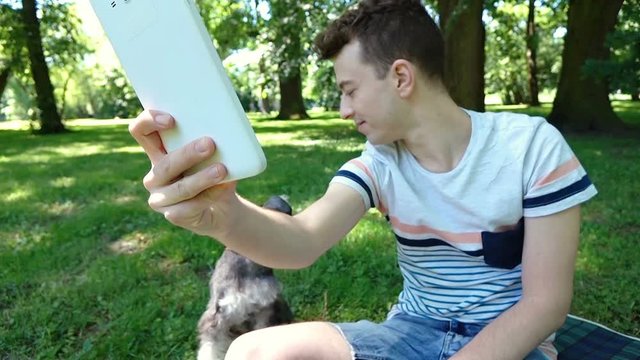 Happy boy doing photos on tablet with his dog while sitting in the park, steadycam shot
