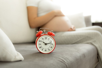 Concept of waiting for baby. Alarm clock against pregnant woman