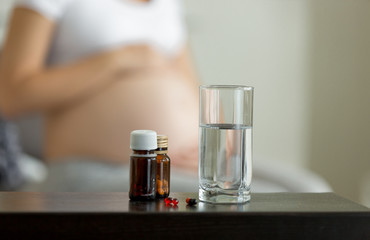 Conceptual photo of pregnancy healthcare. Medicines on table next to pregnant woman