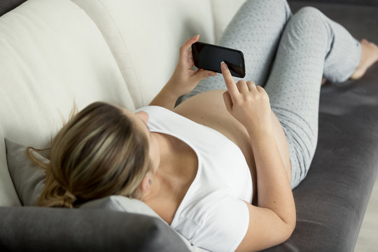 Young pregnant woman lying on sofa and looking at ultrasound embryo image