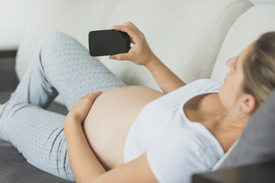 Closeup shot of pregnant woman relaxing on sofa and using mobile phone