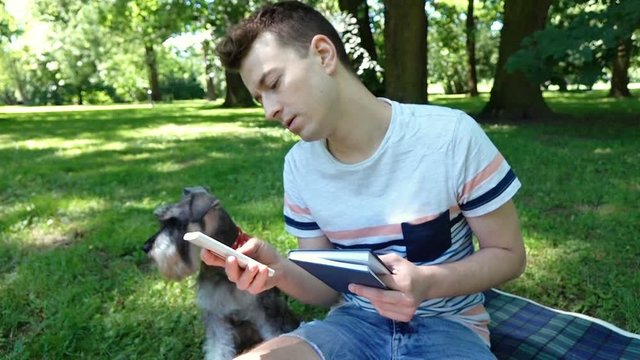 Boy receives message on smartphone while reading book in the park, steadycam shot
