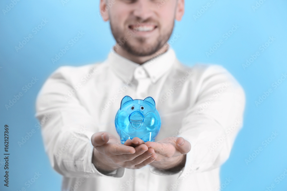 Sticker happy young man holding piggy bank on light background