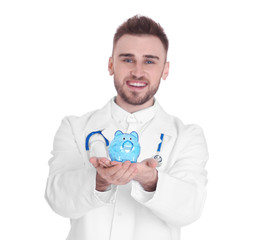 Happy young doctor holding piggy bank on white background