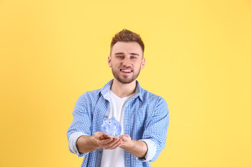 Happy young man holding piggy bank on color background