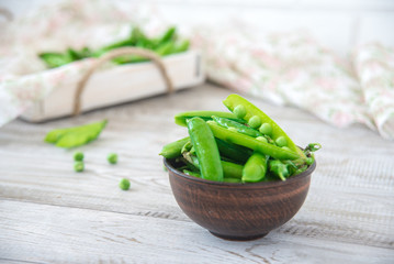Pods of green peas outside in a small bowl on a wooden table