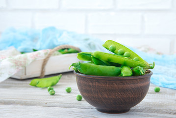 Pods of green peas outside in a small bowl on a wooden table
