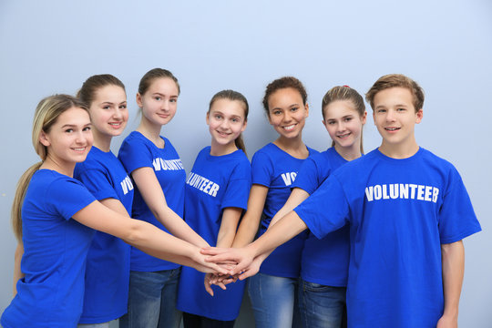 Team of volunteers putting their hands together as symbol of unity, on color background