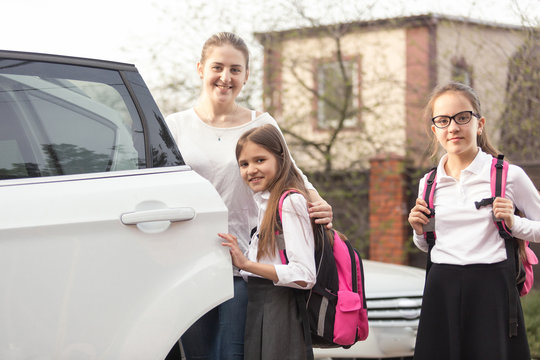 Happy mother and two girls with school bags posing at the car