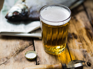 A glass beaker with beer next to a large dried fish bream on an old wooden background