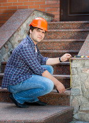 Smiling male worker measuring stone staircase with measuring tape