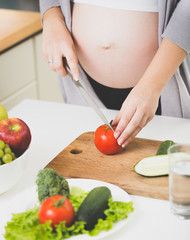 Obraz na płótnie Canvas Closeup image of pregnant woman cutting fresh tomatoes for salad