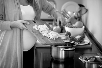 Closeup black and white photo of pregnant woman cooking vegetable soup