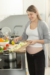Obraz na płótnie Canvas Portrait of smiling pregnant woman putting vegetables in soup