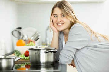 Obraz na płótnie Canvas Portrait of happy smiling woman posing on kitchen and cooking soup