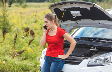 Woman leaning on broken car and calling for help by mobile phone