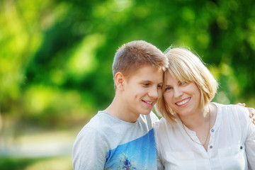 A middle-aged woman and her son teenager are smiling at each other in the park