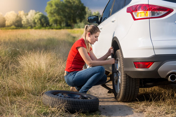 Beautiful woman changing flat tire in field