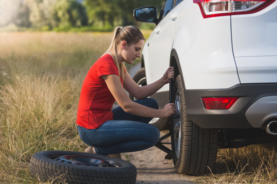 Young Woman Changing Flat Tire In Field