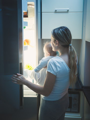 Fototapeta na wymiar Mother with her baby opening refrigerator at late night