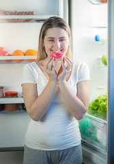 Portrait of woman eating big donut on kitchen at night