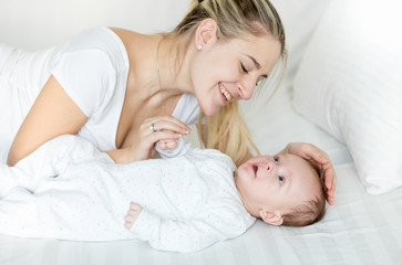 3 months old baby boy lying on bed with young smiling mother