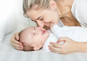 Portrait of happy young mother kissing her baby boy on bed