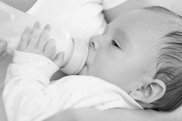Black and white closeup portrait of cute 3 months old baby boy drinking milk from bottle